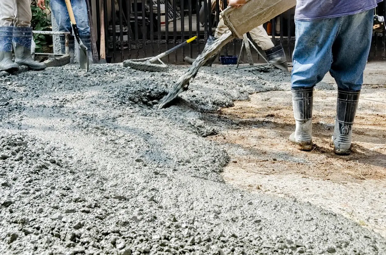 A person using a shovel to spread cement on the ground.